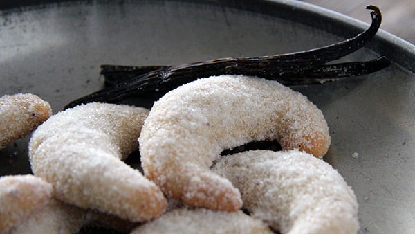 Vanillekipferl mit Puderzucker und Vanilleschote auf Metallteller