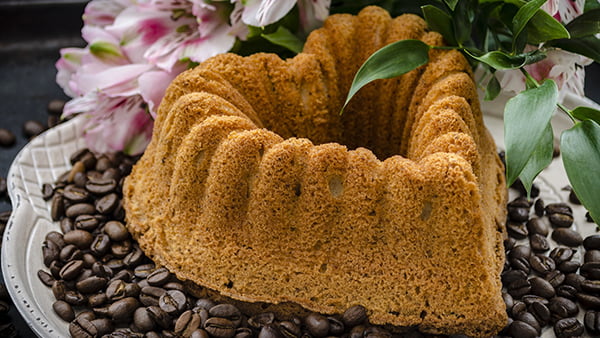 Gugelhupfkuchen in Herzform angerichtet auf einem Teller mit Kaffeebohnen