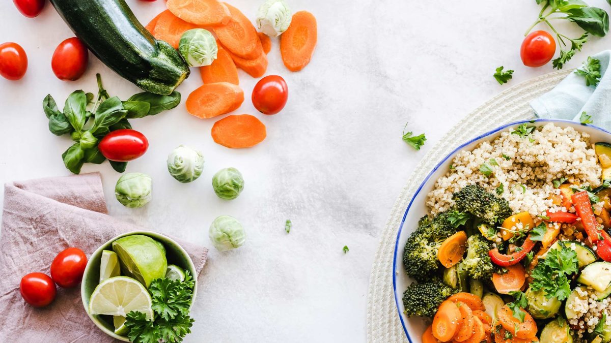 Slow Food Header am beispiel mit einer schüssel voll couscous mit gemüse und lose liegendem gemüse wie zucchini und rosenkohl auf einer weißen unterlage