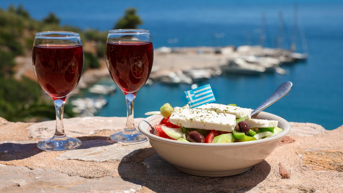 zwei weingläser neben einer salatschüssel mit griechischem meer im hintergrund