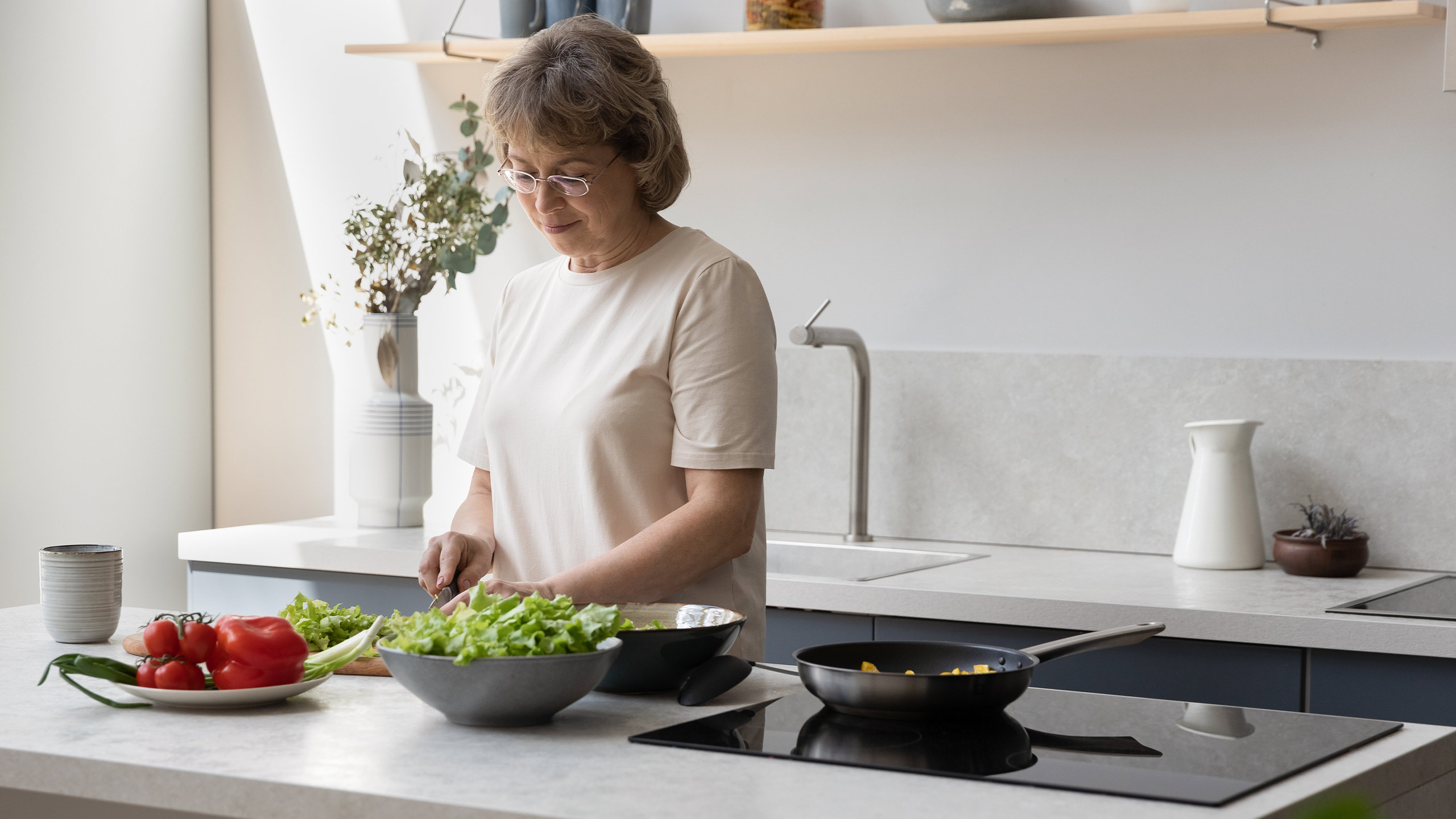 frau steht in einer weiß-grauen küche und schneidet salat