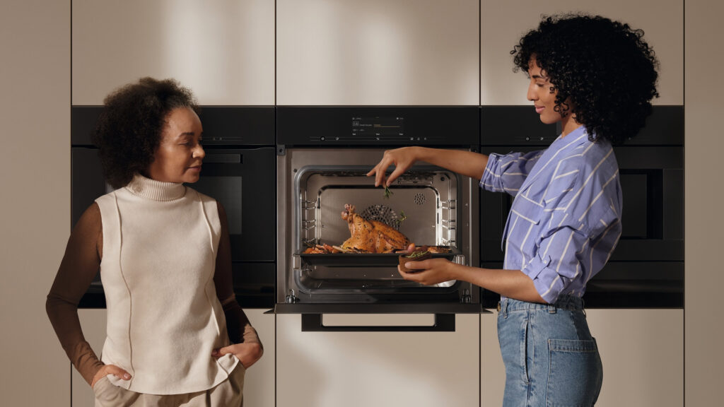 zwei frauen stehen vor einem miele dampfbackofen mit knusprig gegartem fleisch