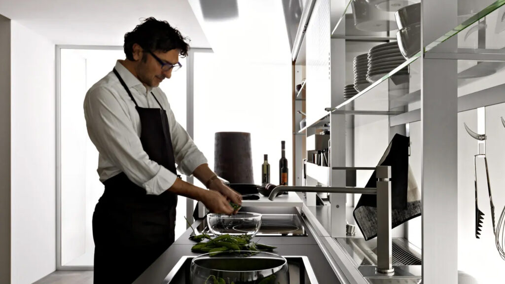 mann mit kochschürze bereitet gemüse in einer glasschüssel vor und steht in einer valcucine küche