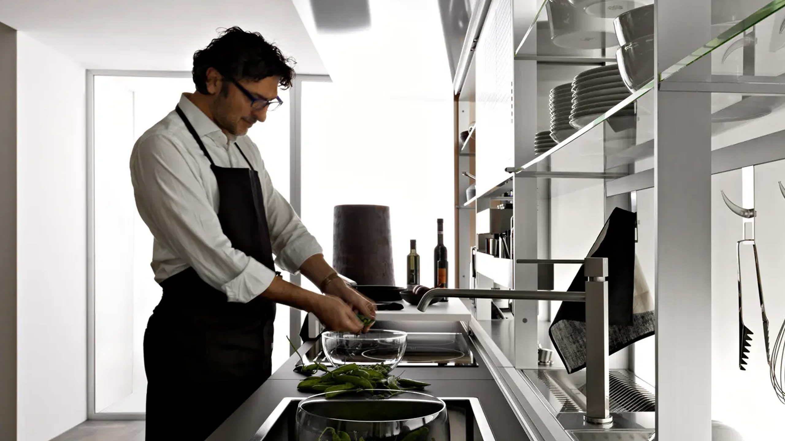 mann mit kochschürze bereitet gemüse in einer glasschüssel vor und steht in einer valcucine küche