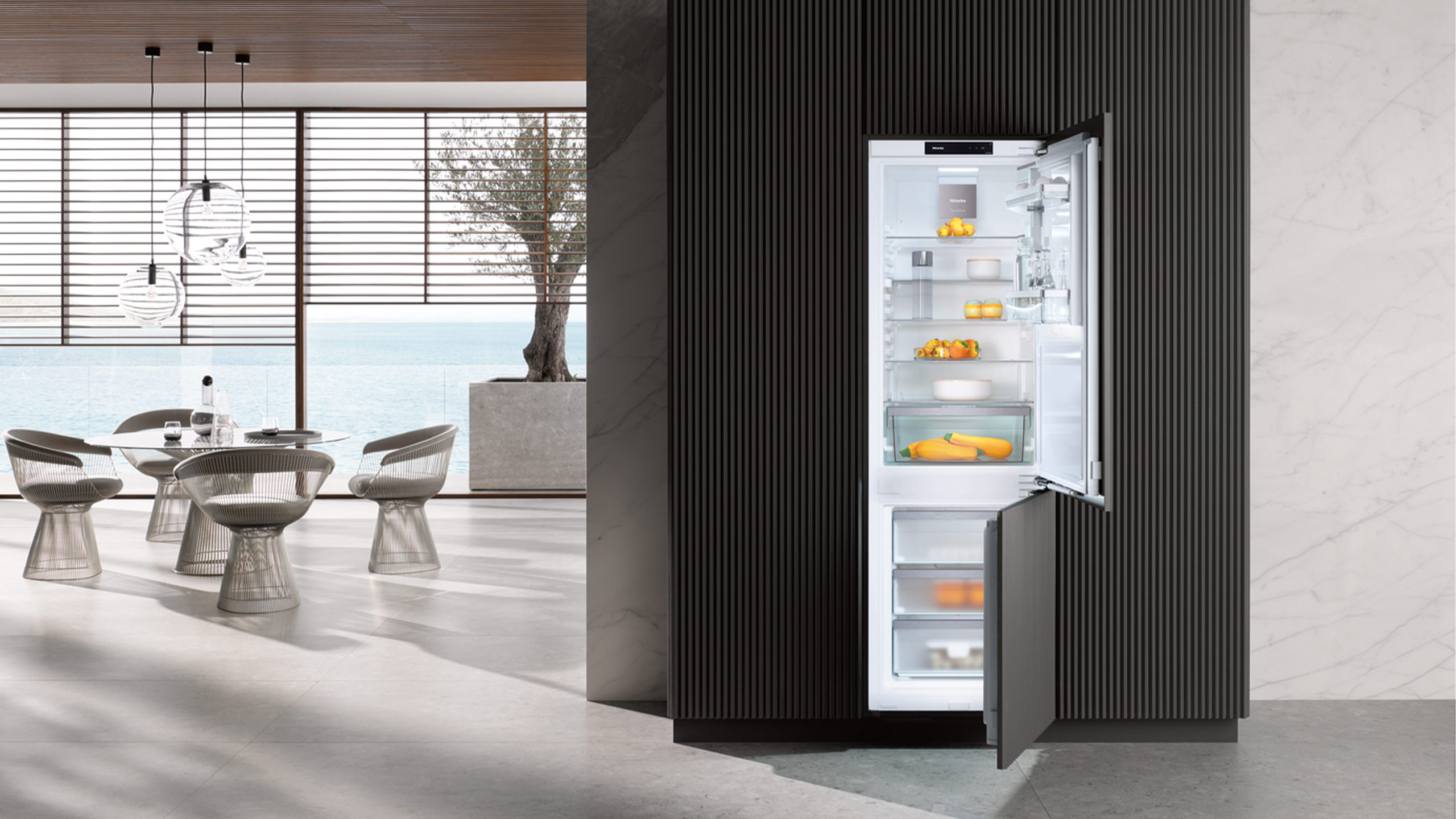 geöffnete miele kfn 7734 c kühl-gefrierkombination in einer küche mit rundem esstisch und meerblick