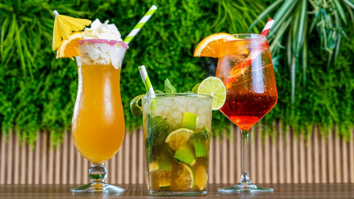 drei bunte sommer cocktails vor einer grünen pflanze